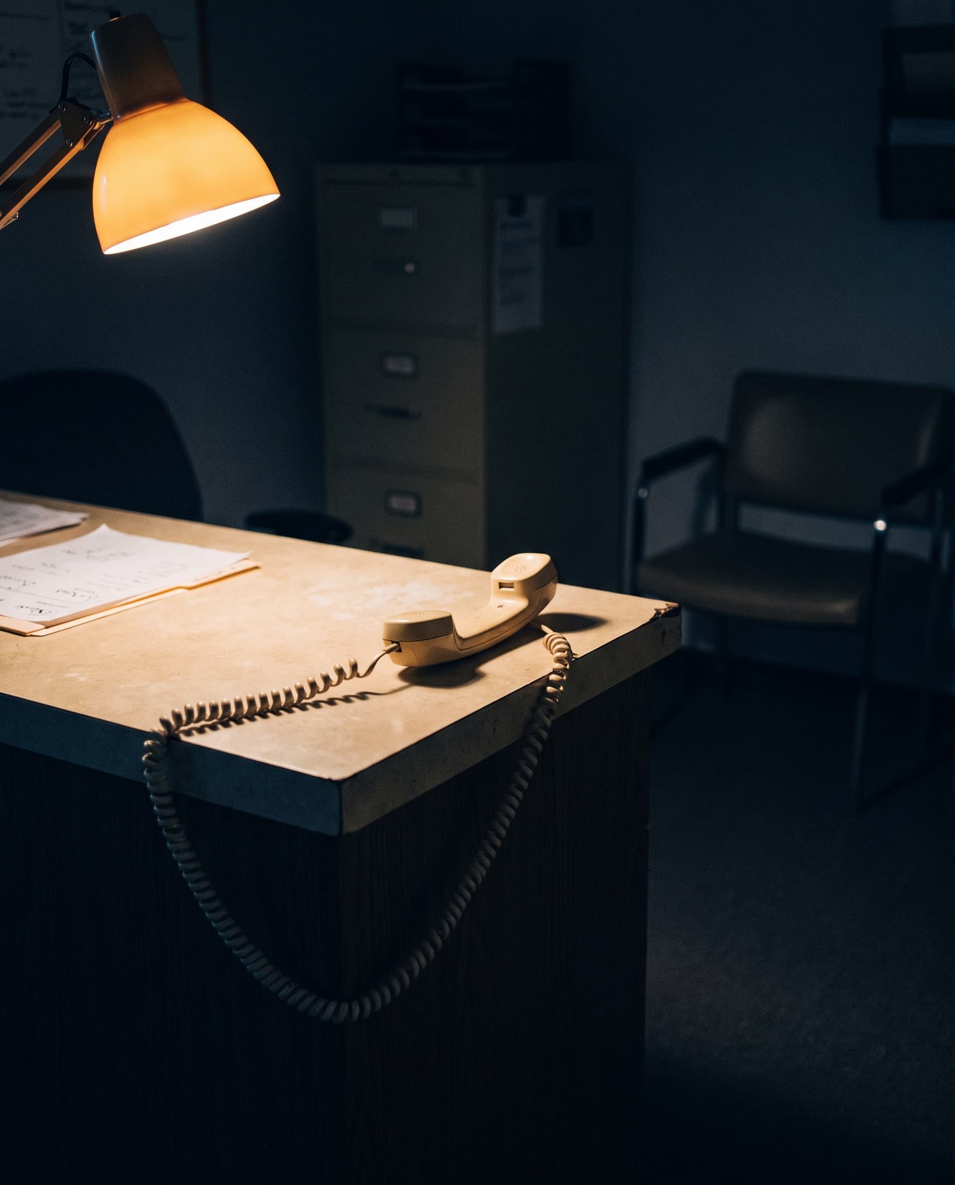 A reception counter after closing, the handset off its cradle under a desk lamp.